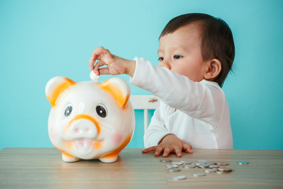 Ein Kleinkind steckt Münzen in ein Sparschwein