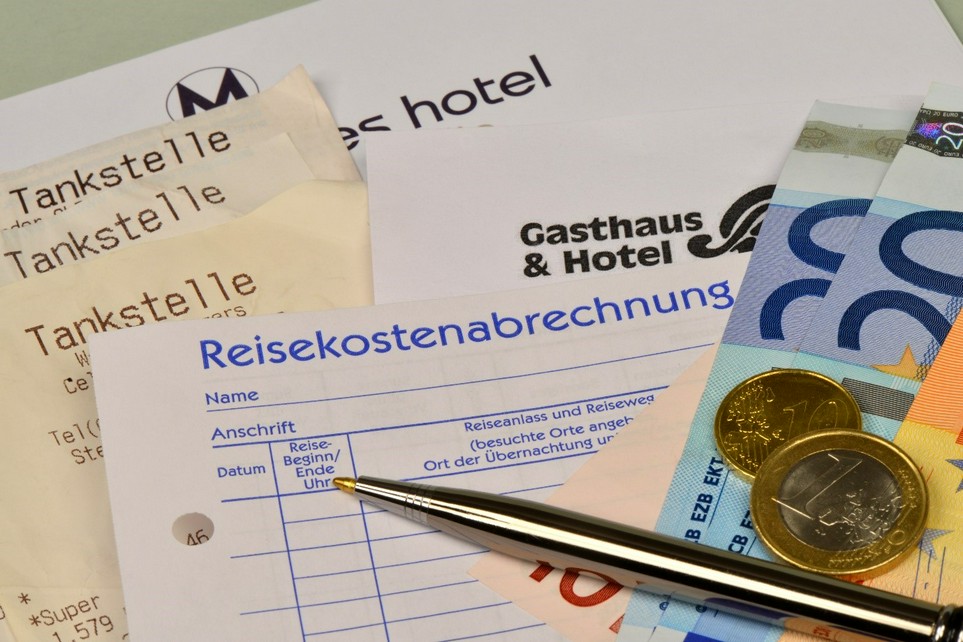 Belege für Hotelübernachtungen und Quittungen von Tankstellen liegen vorbereitet sortiert unter einer Reisekostenabrechnung, Kugelschreiber, Geldscheinen und Münzen als Vorbereitung für die Steuererklärung.